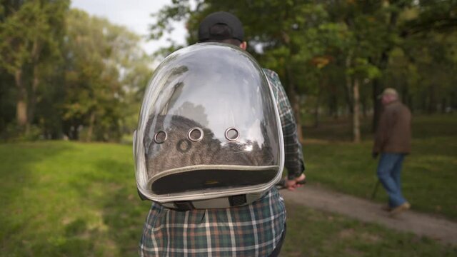 Caucasian male cat lover always travels on bicycle with his pet. Transportation of gray young cat in transparent backpack with porthole on bike. Animal care, people and pets journey awheel theme
