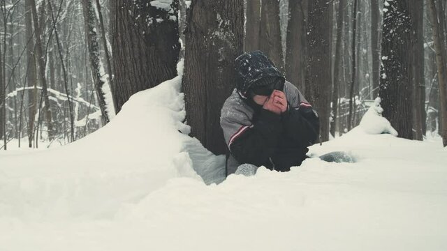 Caucasian man wearing sunglasses sits waist deep in snow next to a tree and freezes. The concept of extreme tourism, injuries during the expedition and harsh, cold, Siberian winters
