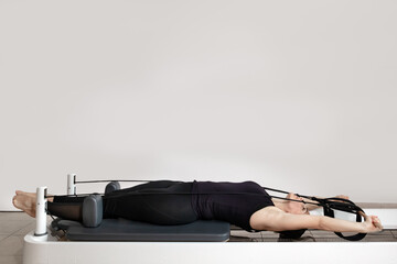 A woman doing pilates exercises pulling elastic bands on a reformed bed.