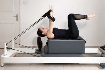 A woman doing pilates exercises pulling elastic bands on a reformed bed.