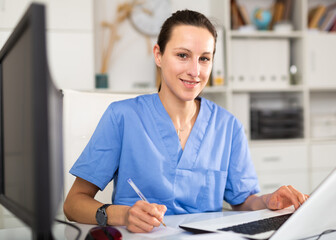 Woman doctor sitting at workplace with computer in her office