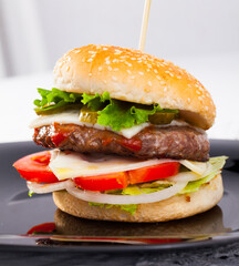 Delicious burger with cheese, tomato, pickled cucumbers, onion and lettuce 