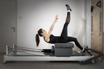 A woman doing pilates exercises with a wooden stick on a reformer bed.