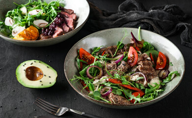Fresh salads with avocado, beef steak, tomatoes, green leaves, arugula, spinach, chicken breast and sweet sauce on dark wooden background. Healthy food, clean eating, closeup