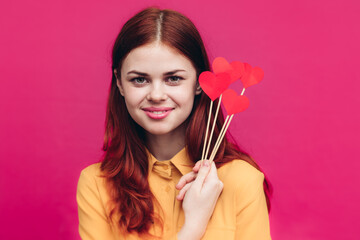 Fototapeta premium happy woman with red hearts on stick and yellow shirt pink background