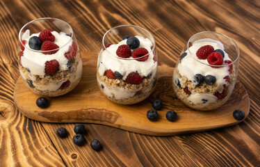 Healthy vegetarian food breakfast dessert made from oats, milk, yogurt, honey, blubbery, raspberries and whole grain cereal in glass. Wooden board, close up