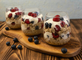 Healthy vegetarian food breakfast dessert made from oats, milk, yogurt, honey, blubbery, raspberries and whole grain cereal in glass. Wooden board, close up