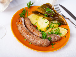 Spicy grilled sausages garnished with boiled potatoes, pepper and fresh parsley