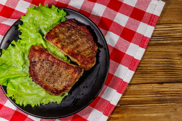 Grilled pork steaks with lettuce leaves on wooden table