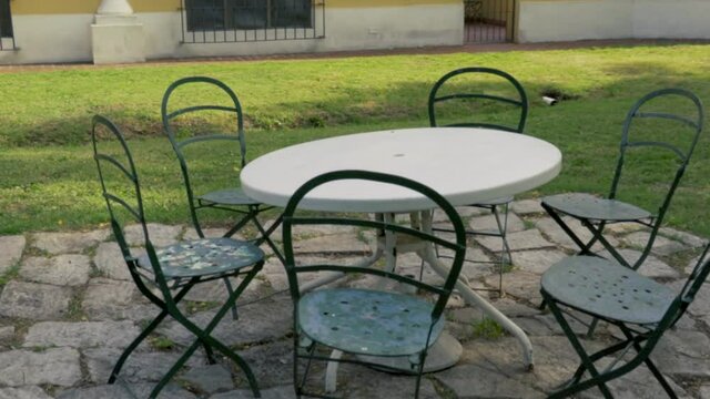 Mesa con sillas met&aacute;licas sobre piso de teja en el jard&iacute;n