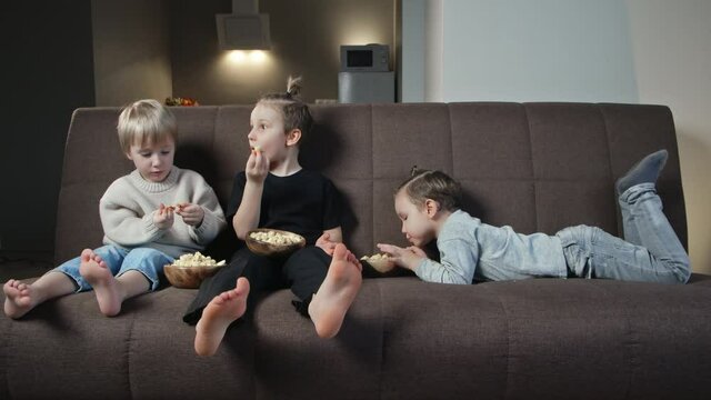 Three brother sit on couch and eat popcorn at home
