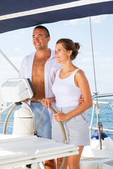 Young man and woman steering pleasure yacht, enjoying romantic sea travel on warm summer day