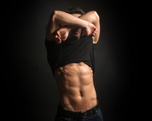Sexy young stylish thoughtful man in black shirt undressing with bare muscular torso and beautiful...
