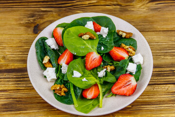 Fresh healthy salad with strawberry, spinach, walnuts and feta cheese on wooden table