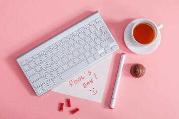 A cup of tea and a keyboard.
Cup of tea with chocolate and keyboard with fools day message on pink background, top view close-up.