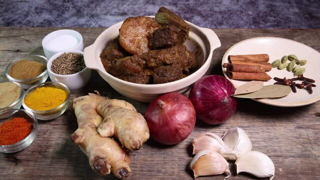 Beef bhuna dry curry with potato in ceramic bowl ingredients chilli cumin coriander turmeric powered salt onion garlic ginger bay leaf cinnamon cardamom clove over rustic wood background 