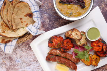 Mixed grill kebab chicken mutton beef prawn fish mint sauce lemon pickled onion bread basket chapati naan tandoori paratha dal lentil fry tadka copper pot on white dish over rustic background