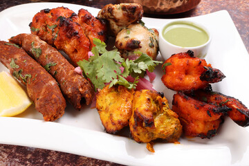 Mixed grill kebab chicken mutton beef prawn fish mint sauce lemon pickled onion coriander on white dish over white background