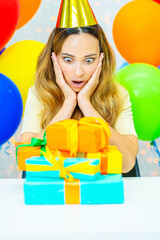 Woman  hugging many gifts in a festive cap on a background of colorful balloons