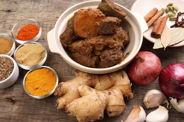 Beef bhuna dry curry with potato in ceramic bowl ingredients chilli cumin coriander turmeric powered salt onion garlic ginger bay leaf cinnamon cardamom clove over rustic wood background