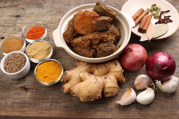 Beef bhuna dry curry with potato in ceramic bowl ingredients chilli cumin coriander turmeric powered salt onion garlic ginger bay leaf cinnamon cardamom clove over rustic wood background