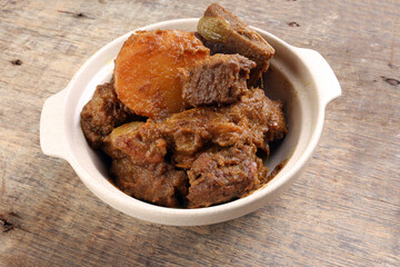 Asian style Beef bhuna dry curry with potato in ceramic bowl over rustic wooden background