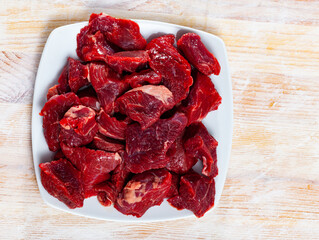 Home cooking. Pieces of fresh raw beef prepared for stewing on wooden table..