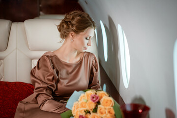 Obraz na płótnie Canvas an attractive blonde woman in an elegant beige dress sits in a comfortable seat on a private jet