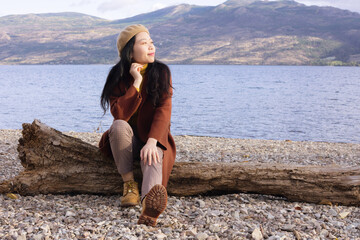 Woman Sitting On A Log By A Lake Gazing At The Sunset 