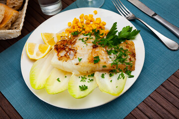 Tasty fried codfish served with endive, greens and corn, Spanish cuisine