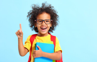 Happy black kid pointing up while standing in blue studio with school copybooks