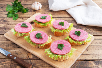 Sandwiches with lettuce leaves and sliced salami sausage on a wooden Board.