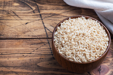 Brown rice raw long grain in a bowl, wooden background copy space, top view.