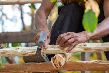 Close-up of a man hammering nails on a eucalyptus wood roof frame. House design using miniature eucalyptus