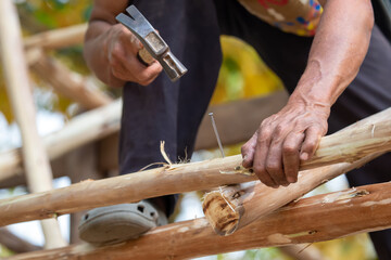 Close-up of a man hammering nails on a eucalyptus wood roof frame. House design using miniature eucalyptus
