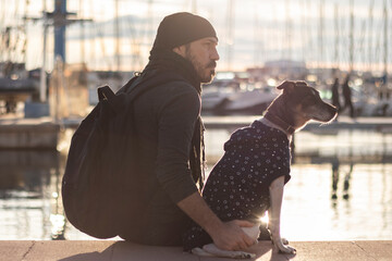 man with his dog sitting on the harbor looking at the horizon. selective focus.