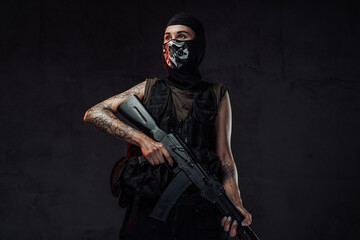 Female soldier poses in dark background holding assault rifle