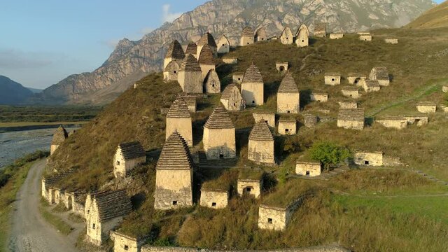 Aerial sideways people tourists walk through city of dead North Ossetia unique ancient burials crypts in form of semi-underground houses on mountain top. Travel tourism Caucasus best landmark. Movie