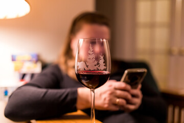Blurred silhouette of a woman behind a wine glass witting in a chain and reading from smartphone