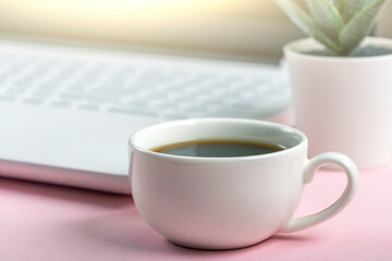 Workspace table with white laptop computer and cup of coffee on pink background. Copy space for text, minimalism.