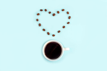 Creative composition: good morning or I love coffee. White cup with black coffee espresso and smile made from beans on blue background. Caffeine boost drink.
