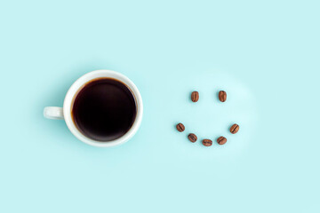 Creative composition: good morning or I love coffee. White cup with black coffee espresso and smile made from beans on blue background. Caffeine boost drink