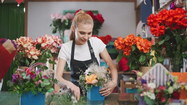 Cheerful female florist decorates a bouquet of flowers in a box, cheerful woman working in a flower and plant shop, multi-colored interior.