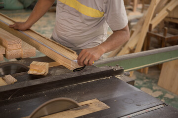 Young worker cutting wood with sawing machine

