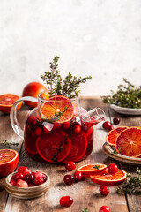 Citrus and berry tea with cranberries, blood oranges and thyme in a glass teapot on wooden table.