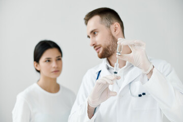 the doctor shows the patient a syringe with a vaccine and protective gloves