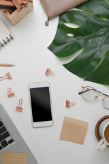 Above view of white office desk with mobile phone, glasses, coffee cup and stationery.