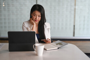 Confident businesswoman sitting at her workplace and holding smart phone.