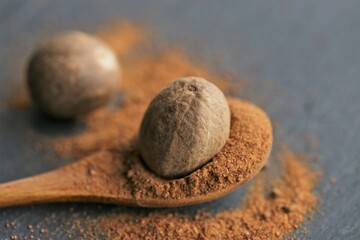 Fototapeta na wymiar Nutmeg spice.Whole and ground nutmeg in a wooden spoon close-up on a black schiffer background.Spices and herbs concept.Food ingredient.Nutmeg powder
