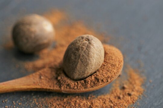 Nutmeg spice.Whole and ground nutmeg in a wooden spoon close-up on a black schiffer background.Spices and herbs concept.Food ingredient.Nutmeg powder